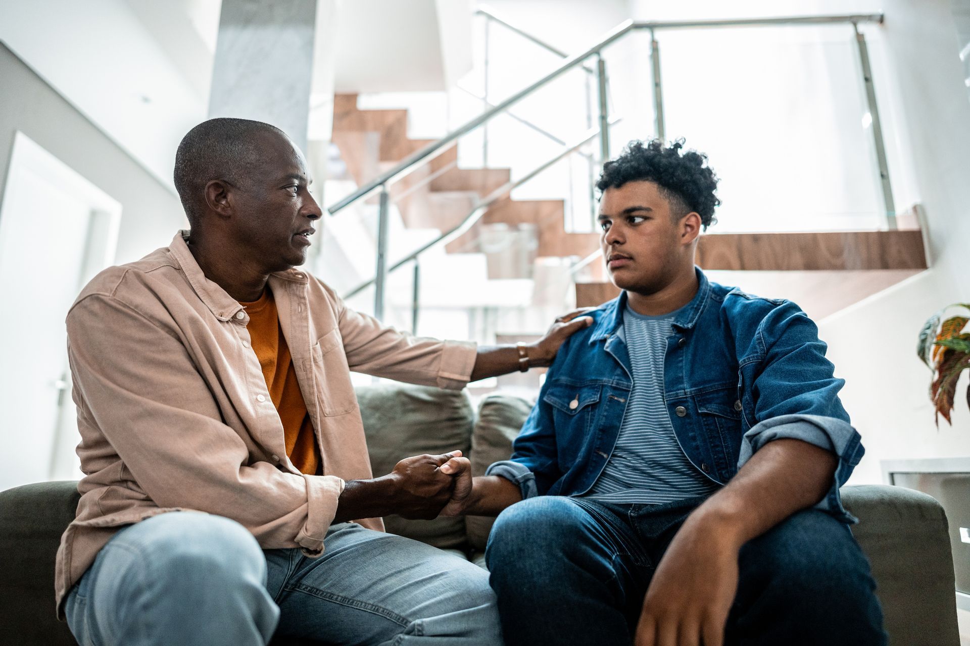 A man is sitting on a couch talking to a young man.