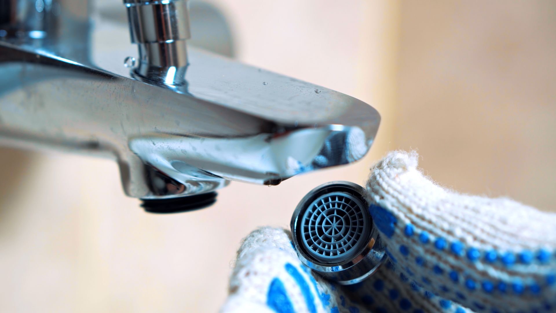 Close-up of a faucet with a gloved hand holding a round showerhead filter underneath it