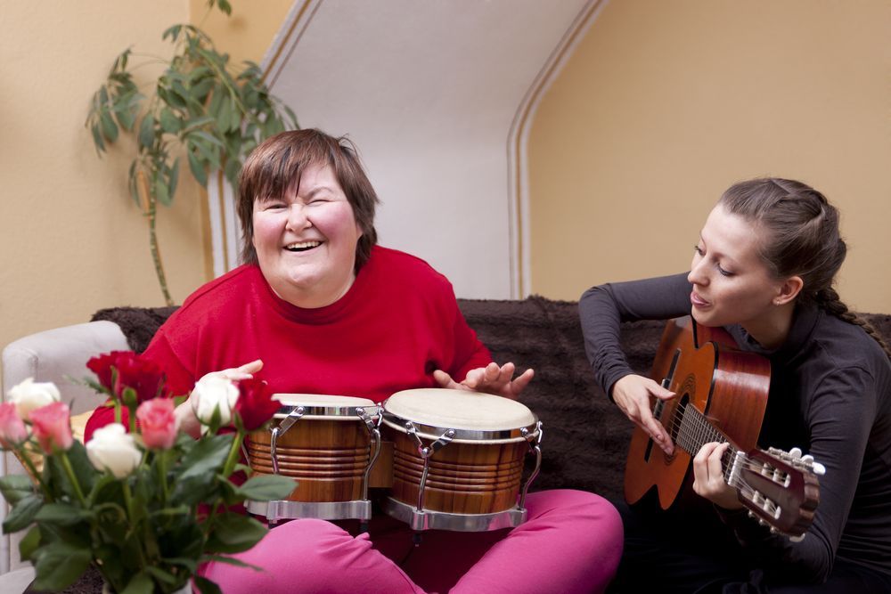 Two Women Are Sitting On A Couch Playing Drums And A Guitar — Coast 2 Coast Disability Support Services in Taree, NSW