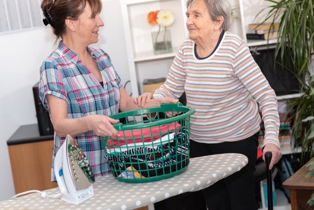 A Woman Is Helping an Elderly Woman Iron Clothes on An Ironing Board — Coast 2 Coast Disability Support Services in Taree, NSW