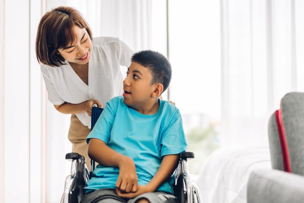 A Woman Is Standing Next to A Boy in A Wheelchair — Coast 2 Coast Disability Support Services in Taree, NSW