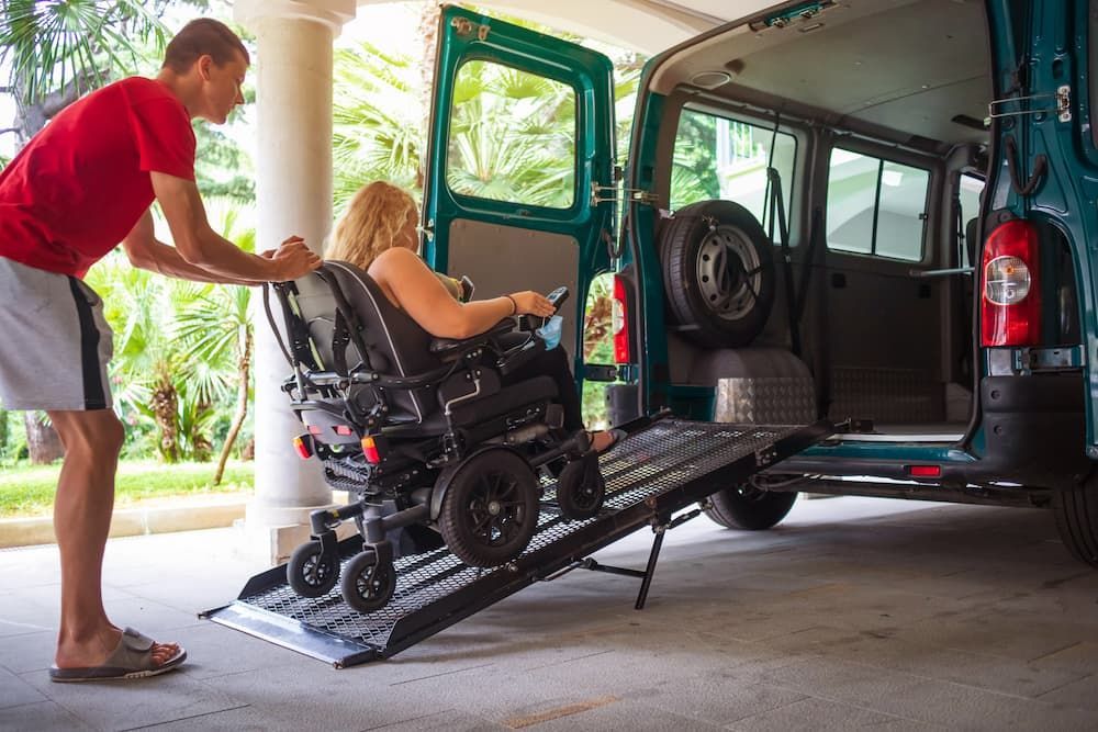 A Man Is Helping a Woman in A Wheelchair Into a Van — Coast 2 Coast Disability Support Services in Taree, NSW