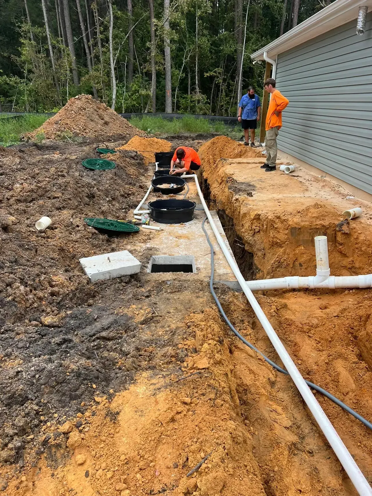 A group of people are working on a septic system in the dirt in front of a house.