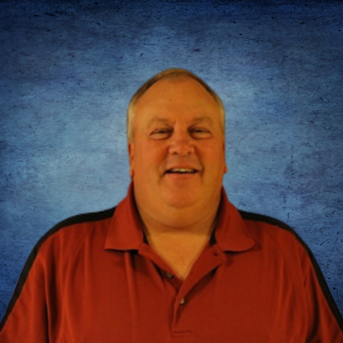 A man in a red shirt is smiling in front of a blue background
