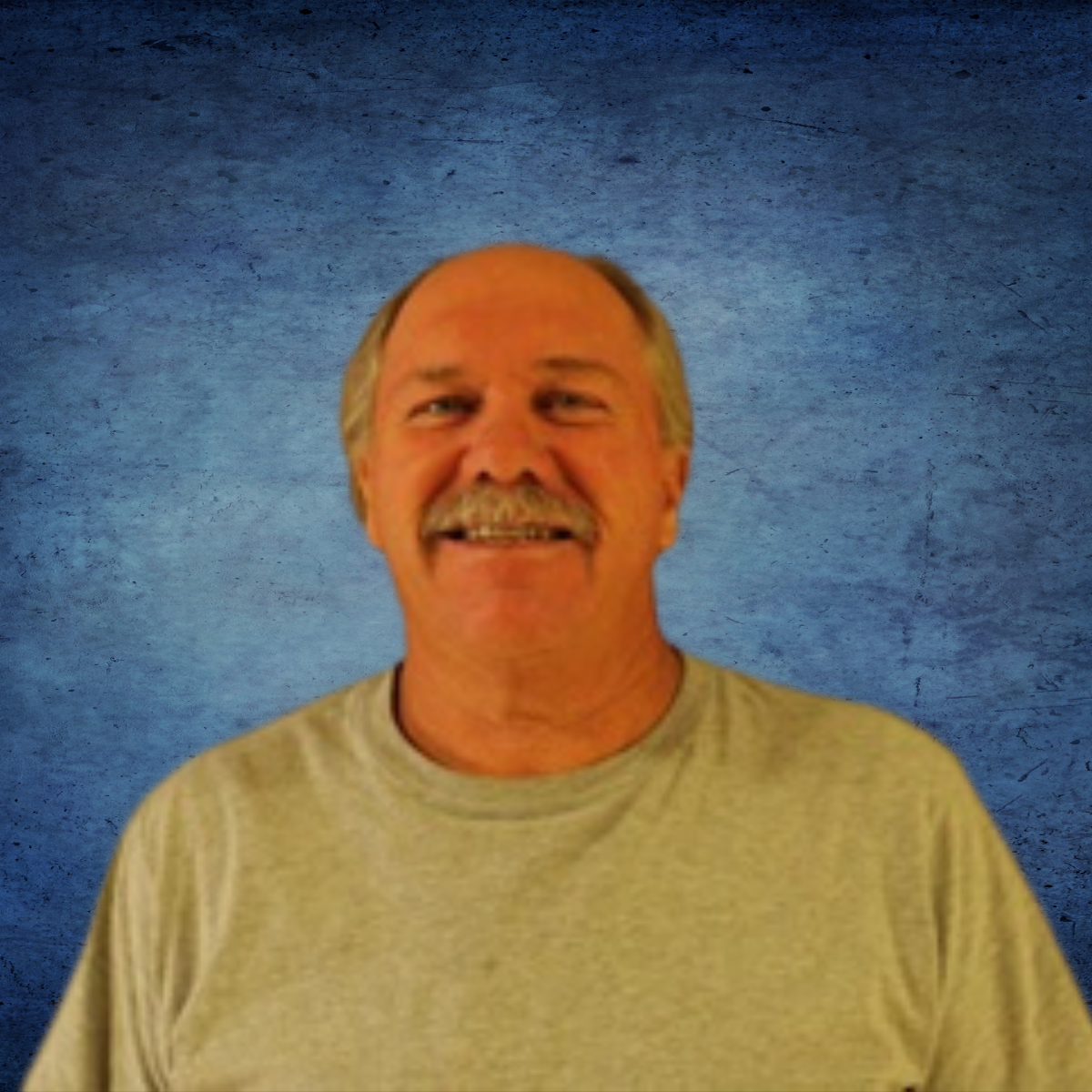 A man with a mustache is smiling in front of a blue background