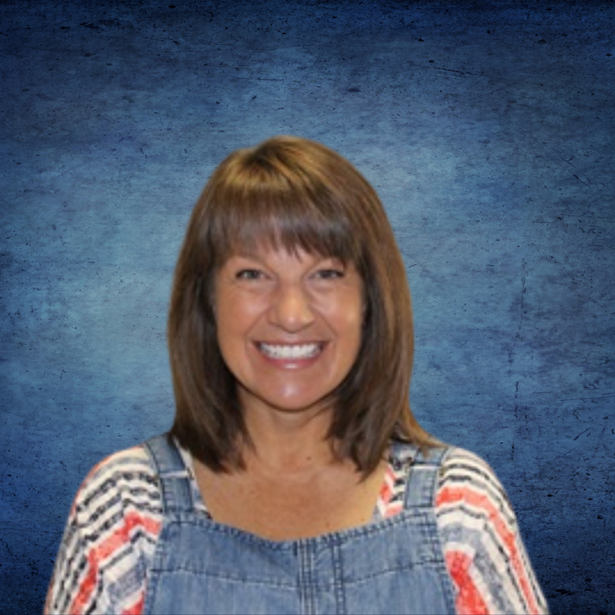 A woman wearing overalls and a striped shirt smiles for the camera
