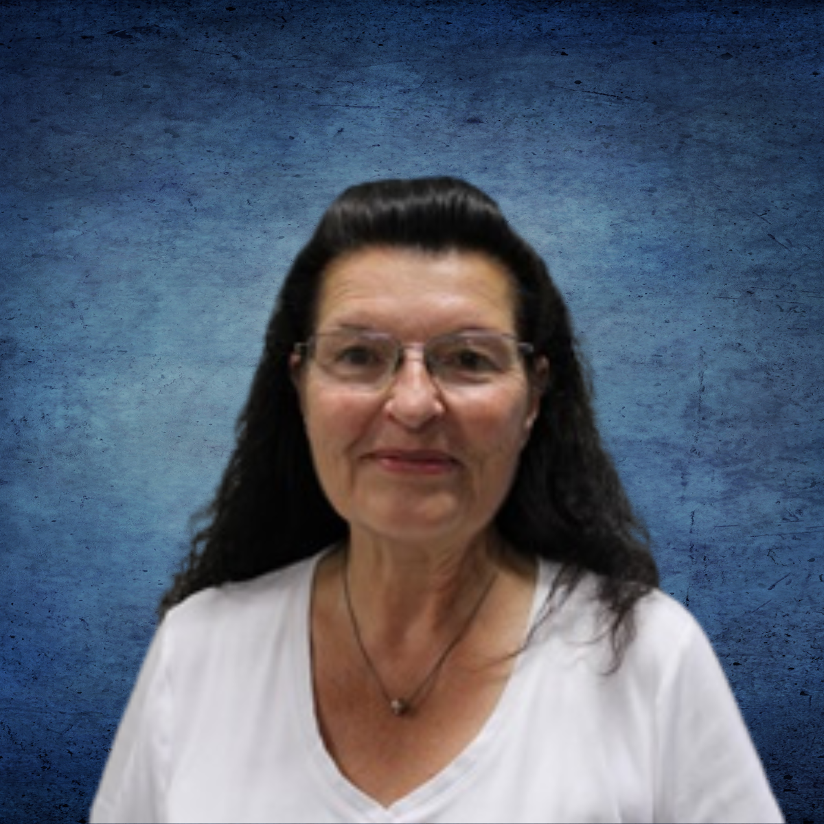 A woman wearing glasses and a necklace is standing in front of a blue wall.