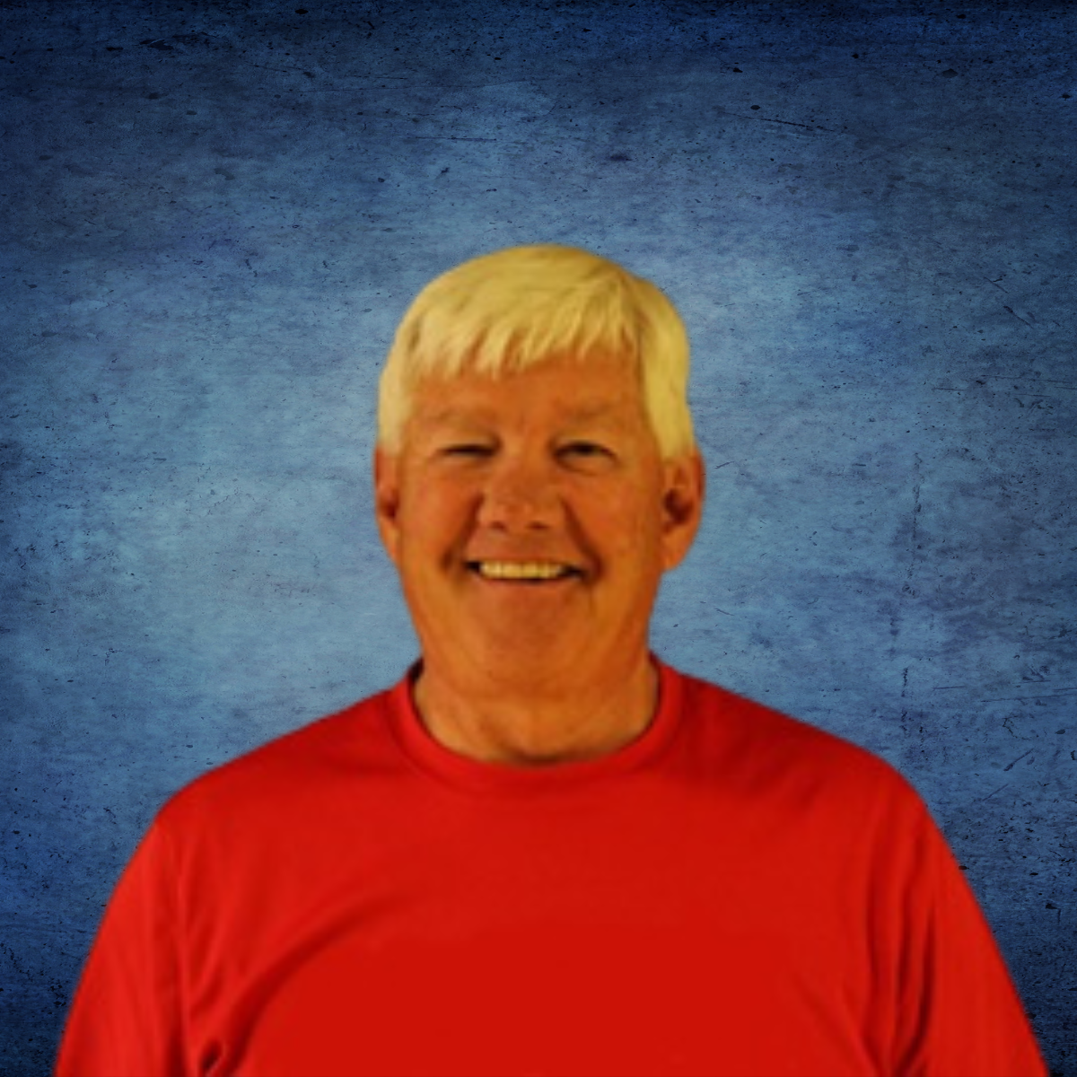 A man in a red shirt is smiling in front of a blue background