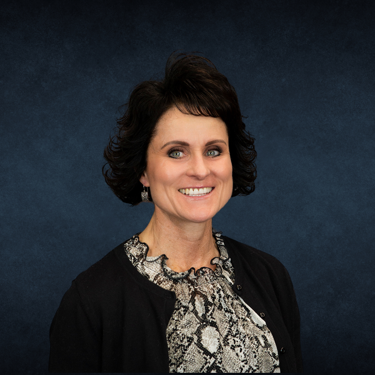 A woman wearing a black jacket and a snake print shirt is smiling for the camera.