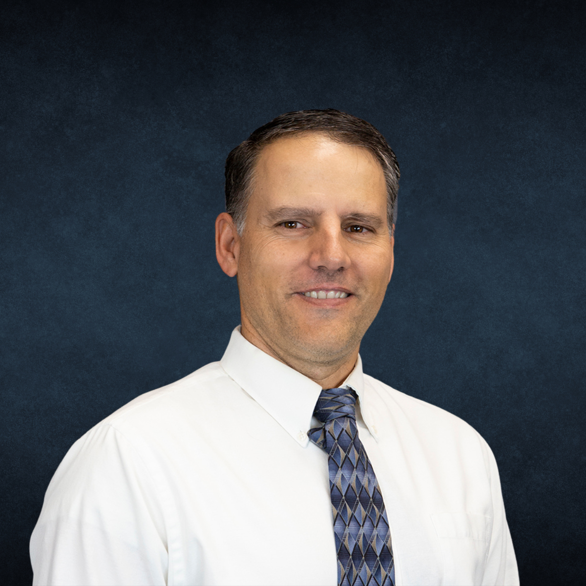 A man in a white shirt and tie is smiling for the camera