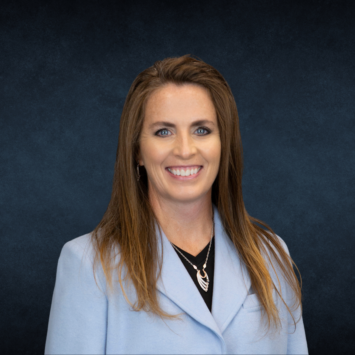 A woman in a blue jacket and necklace is smiling for the camera.