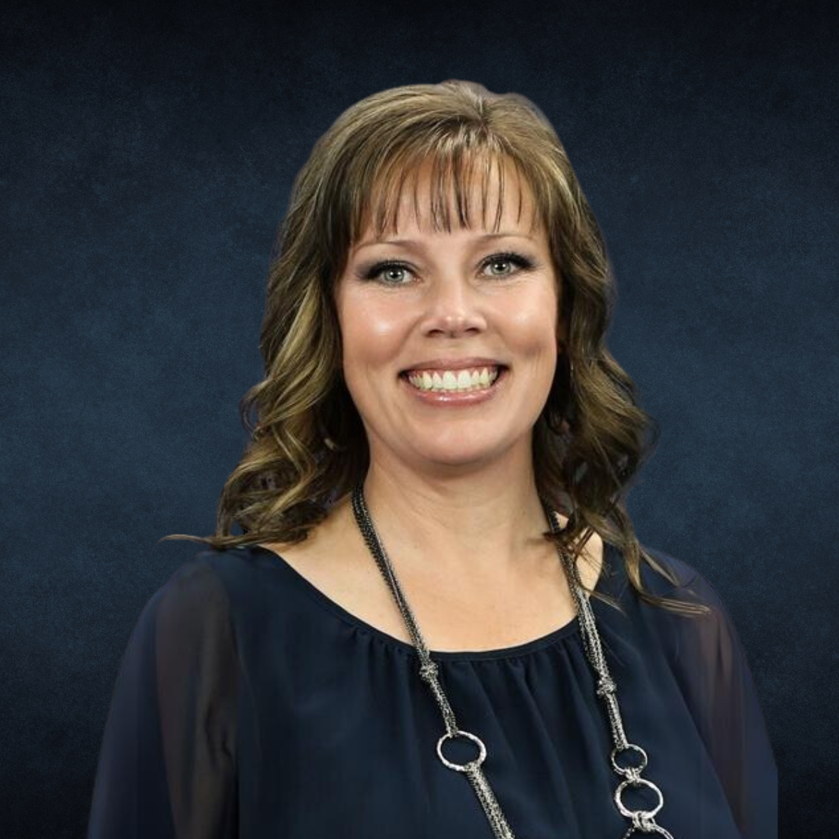 A woman wearing a blue shirt and a necklace smiles for the camera