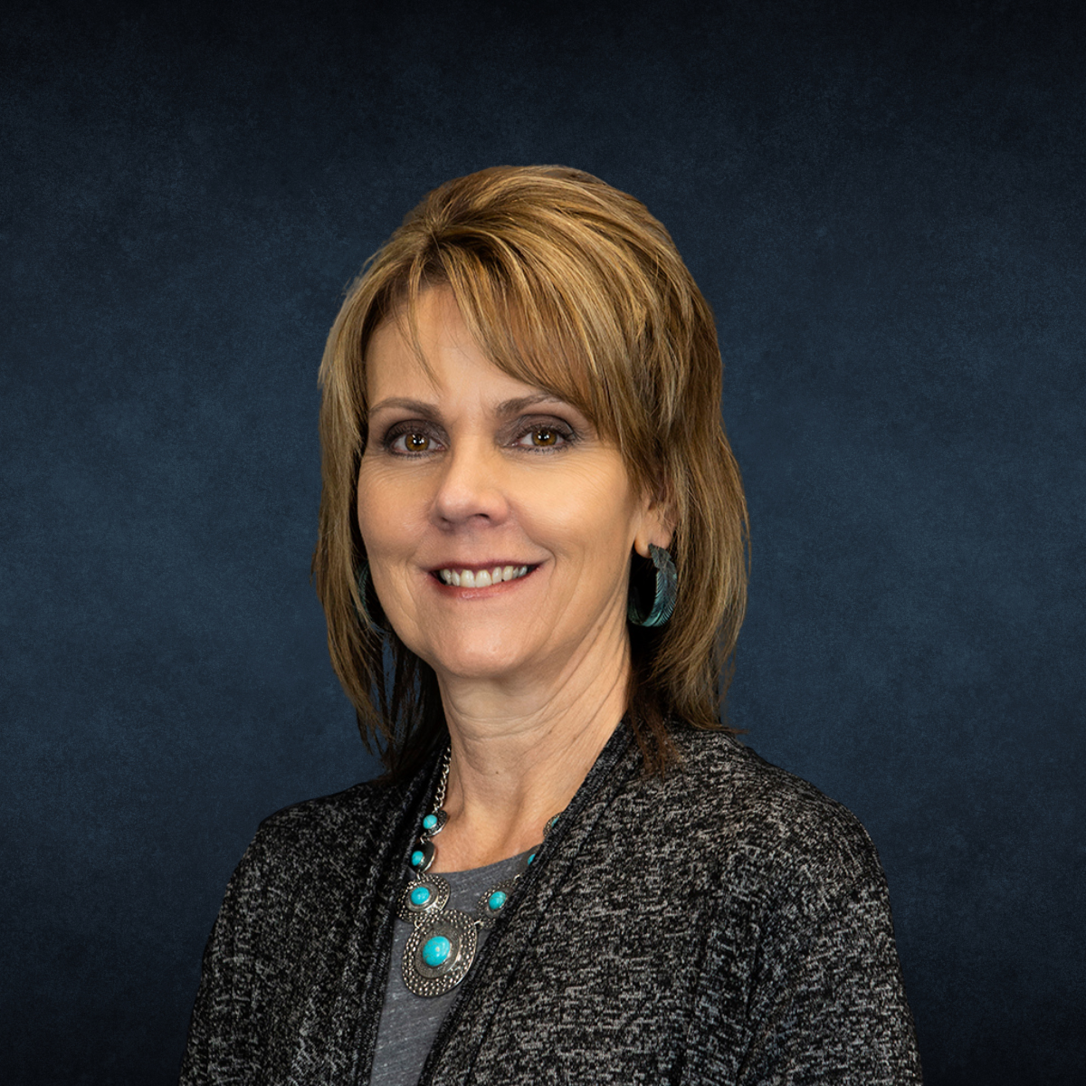 A woman wearing a turquoise necklace and earrings is smiling for the camera.