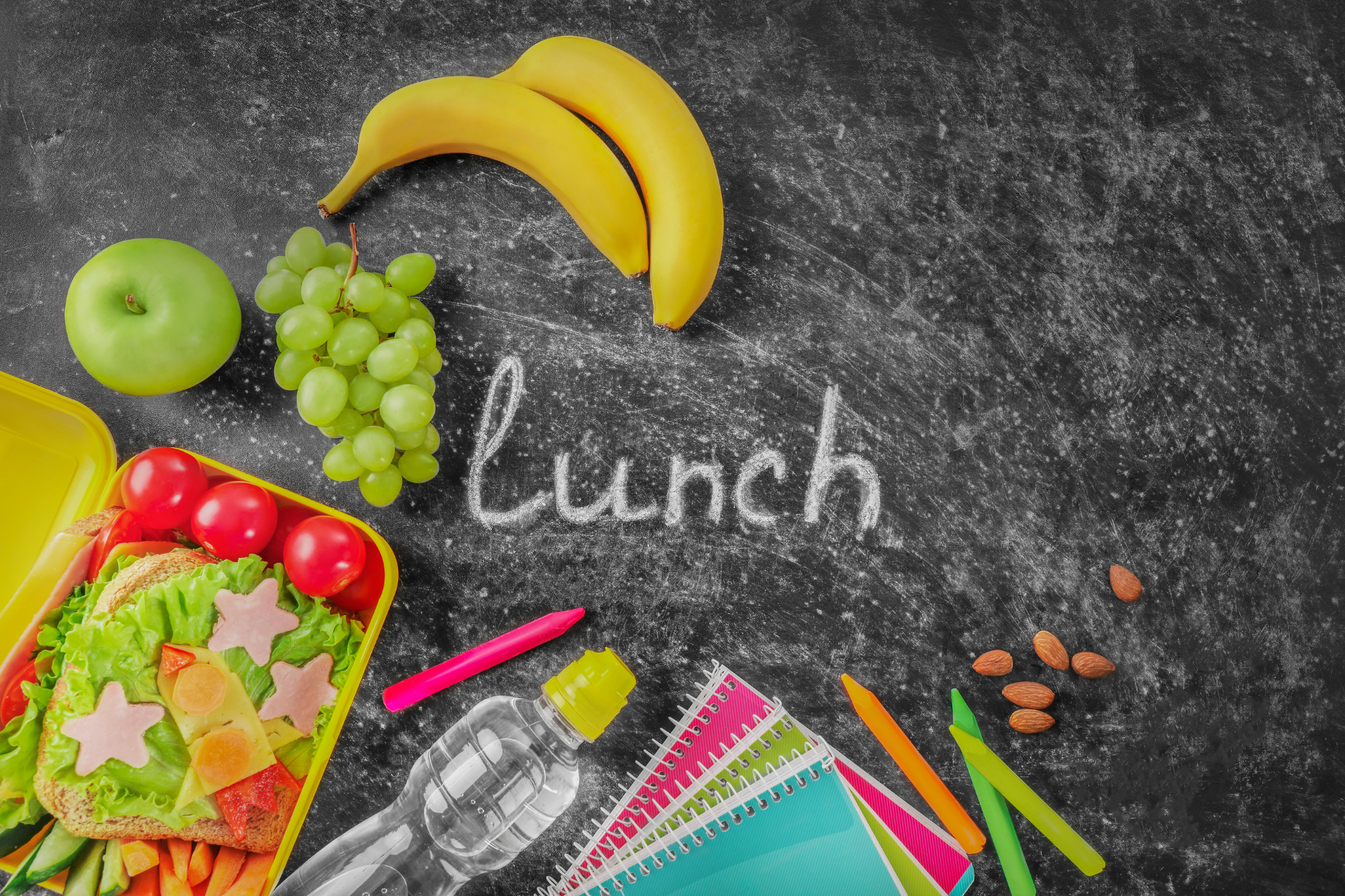 The word lunch is written on a blackboard next to a lunch box filled with fruits and vegetables.
