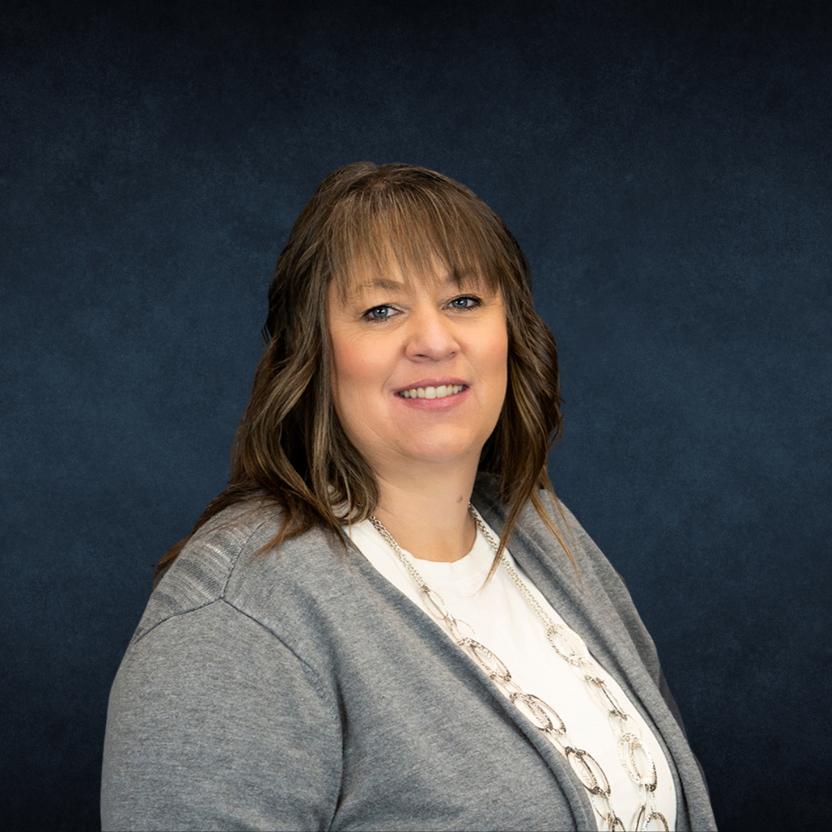 A woman in a grey sweater and white shirt is smiling for the camera.