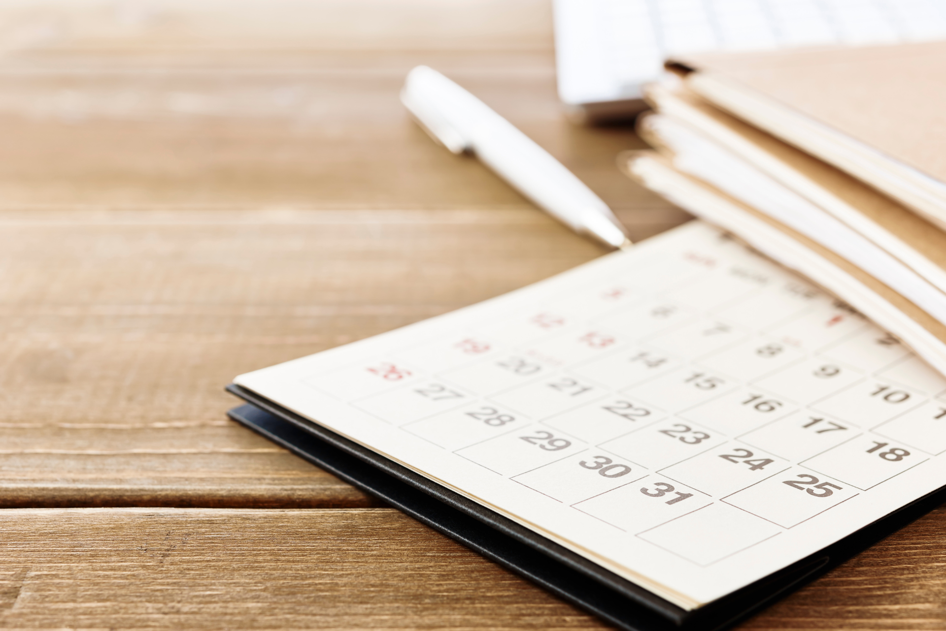 A calendar sits on a wooden table next to a pen
