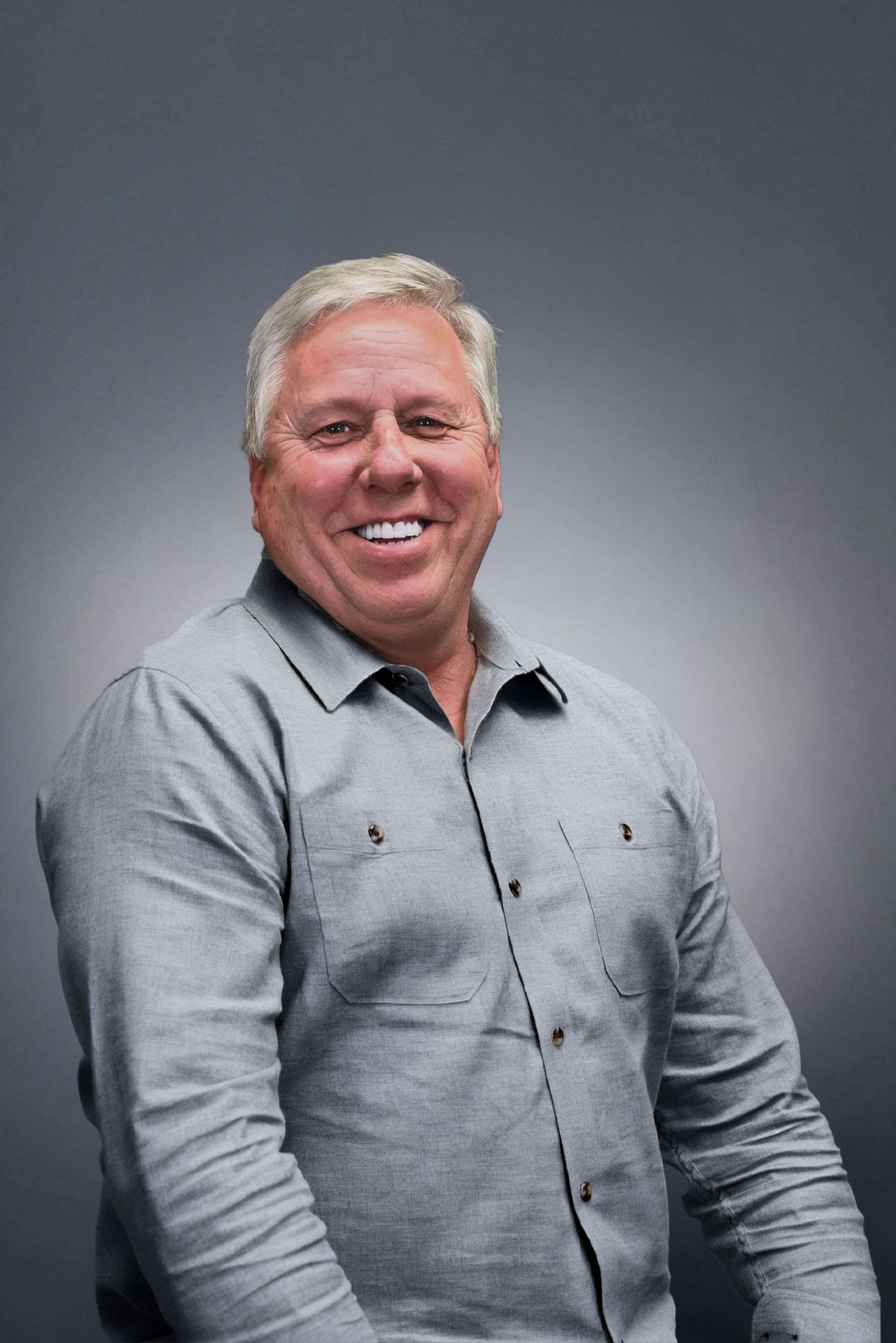 Woman in a teal dress, arms crossed, smiling at the camera against a gray backdrop.