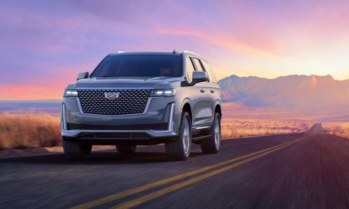 A silver cadillac escalade is driving down a desert road at sunset.