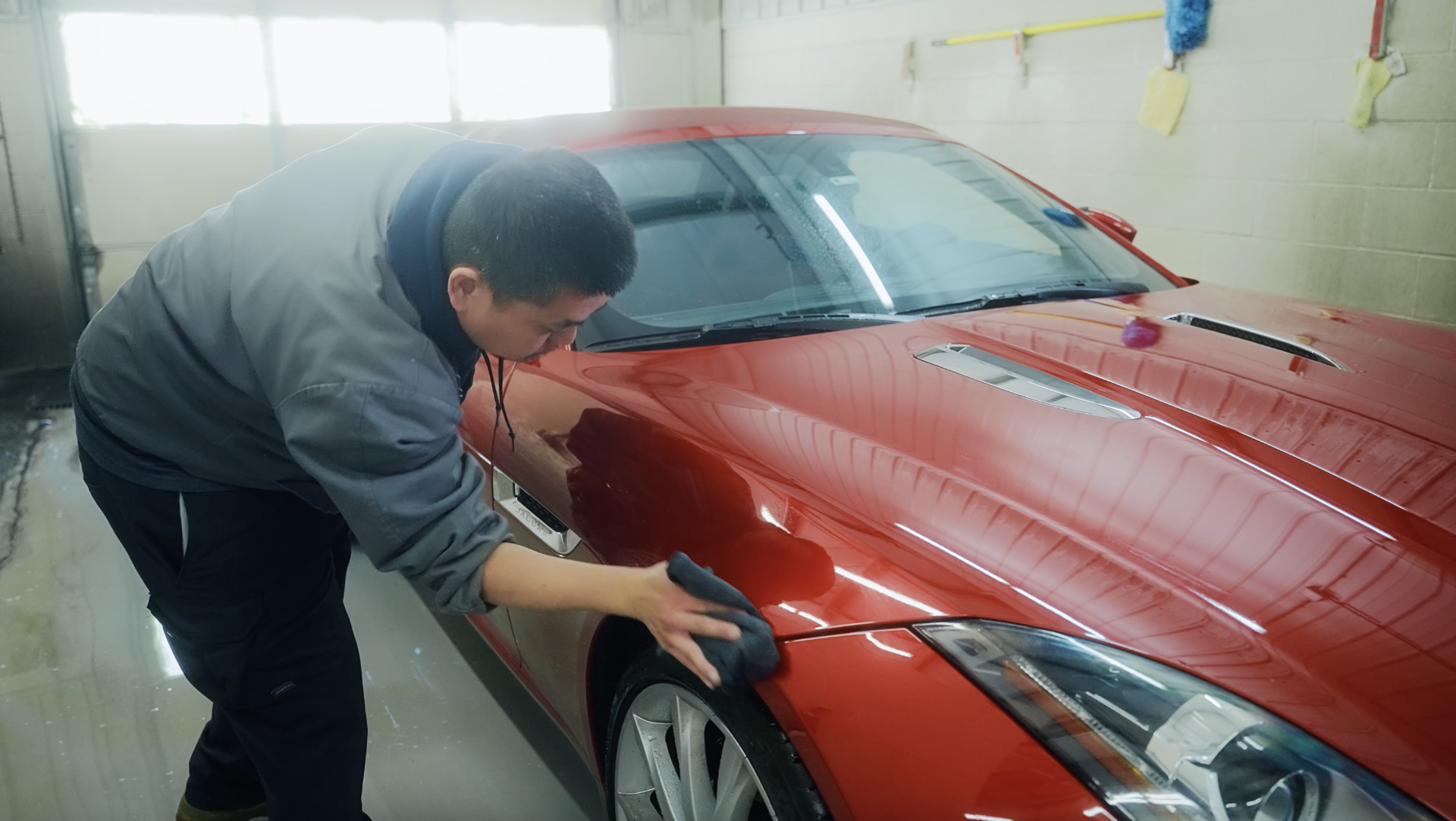 A man is polishing a red car in a garage.