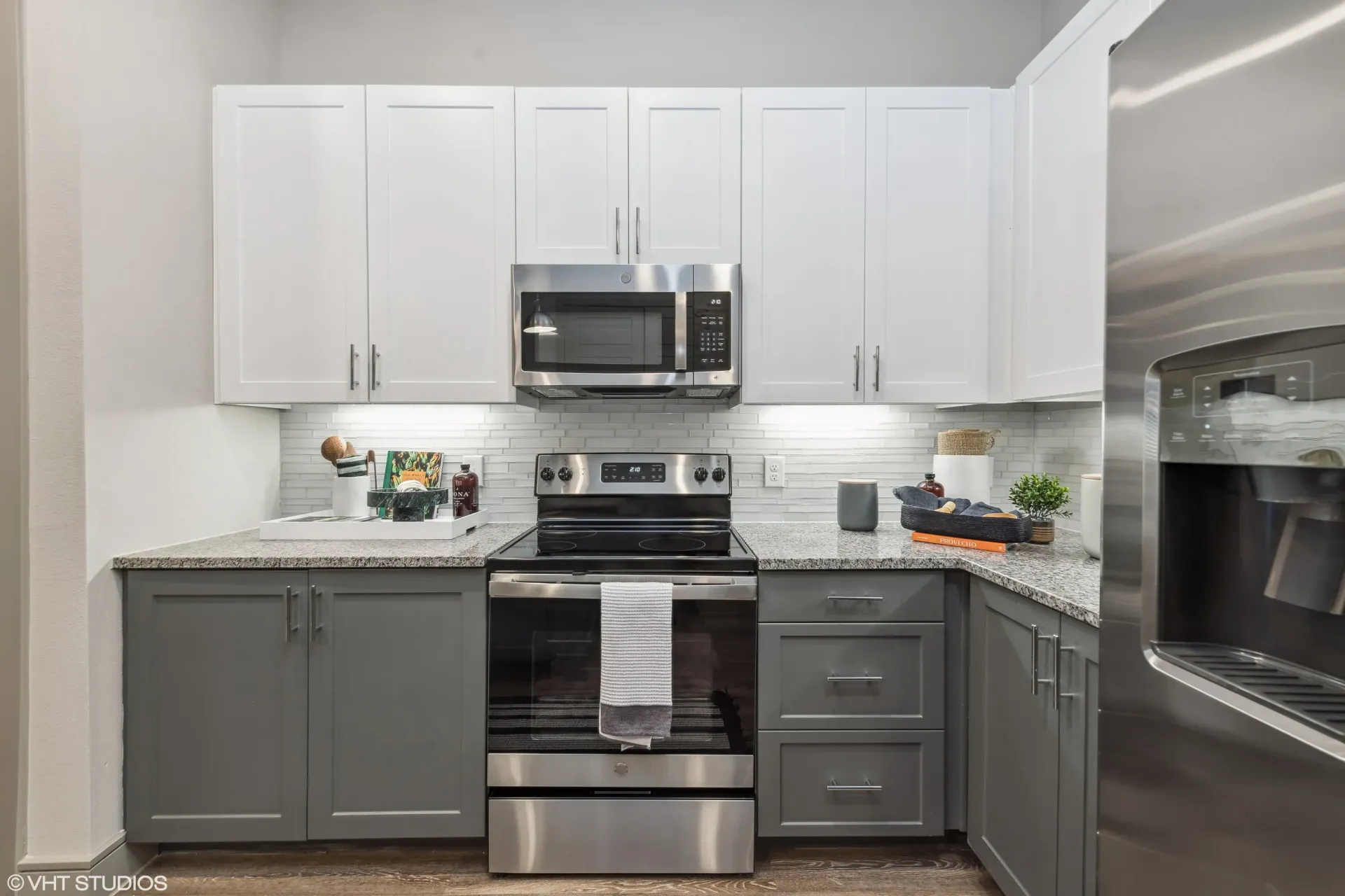 Modern apartment kitchen with white upper cabinets, gray lower cabinets, and stainless steel appliances.