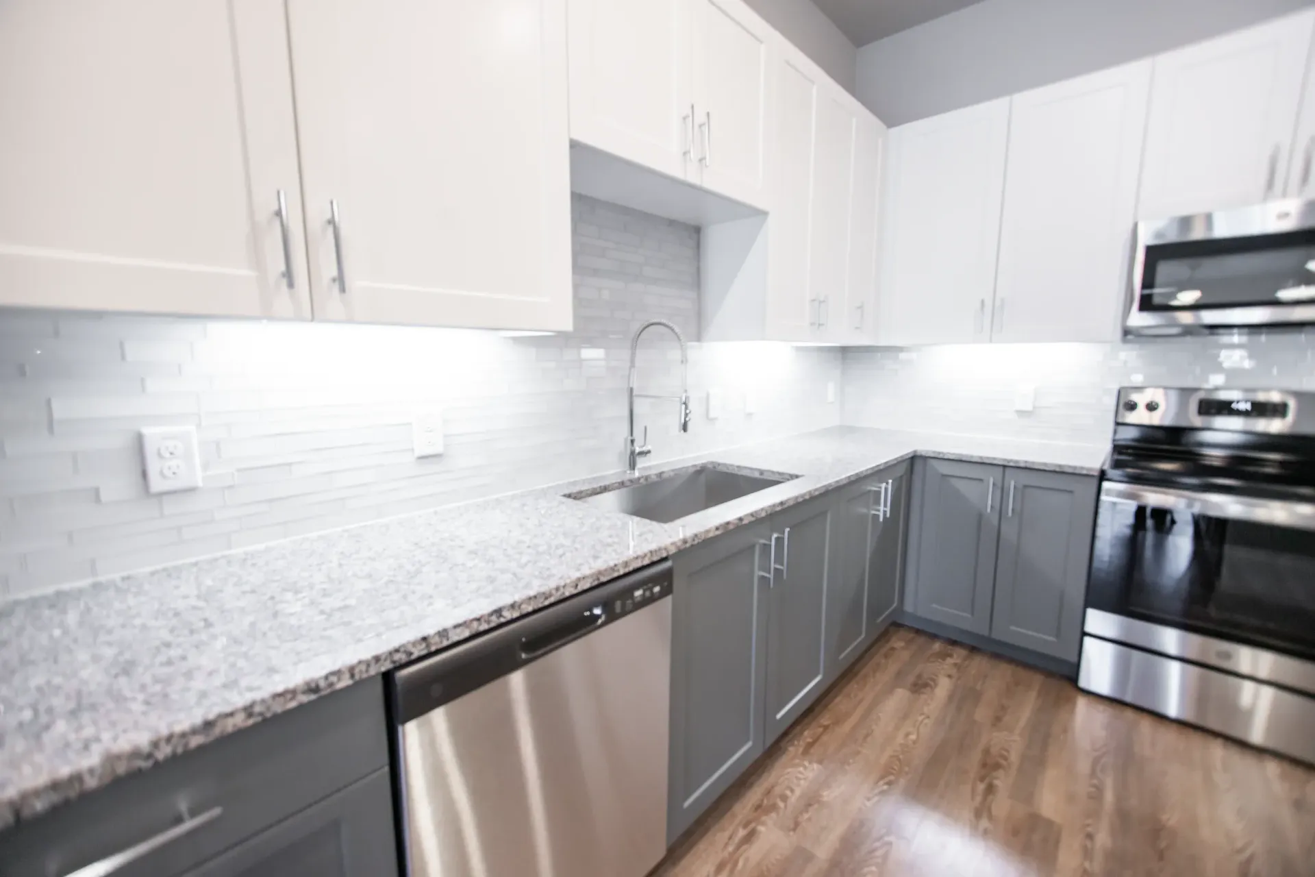 Modern kitchen with white upper cabinets, gray lower cabinets, granite countertops, and stainless steel appliances.