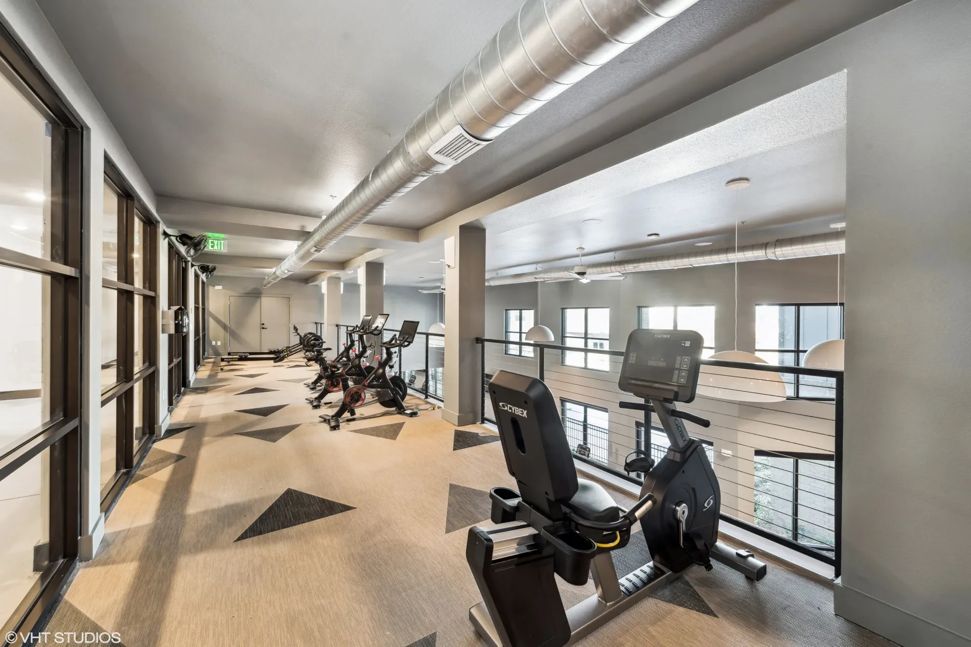 Interior of a modern apartment gym with cardio machines and large windows.
