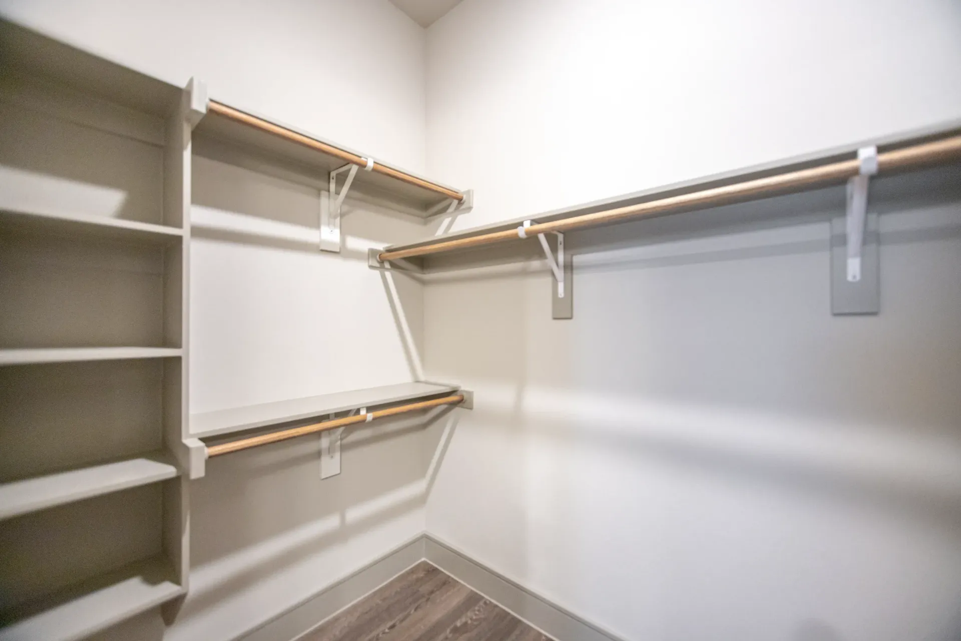 Walk-in closet with white built-in shelves and wooden rod hangers.