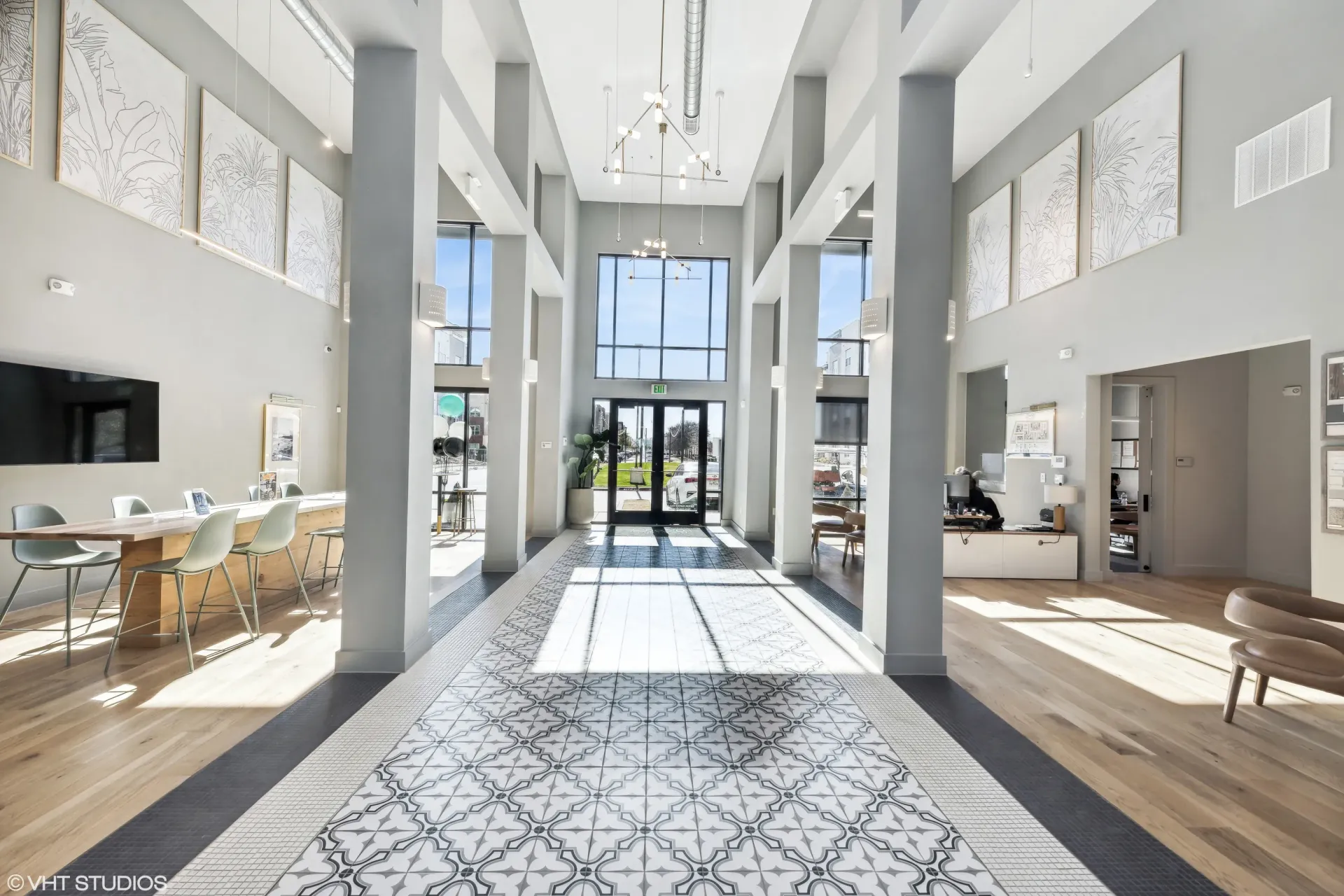 Bright residential lobby with high ceilings, tall pillars, and glass entrance doors.