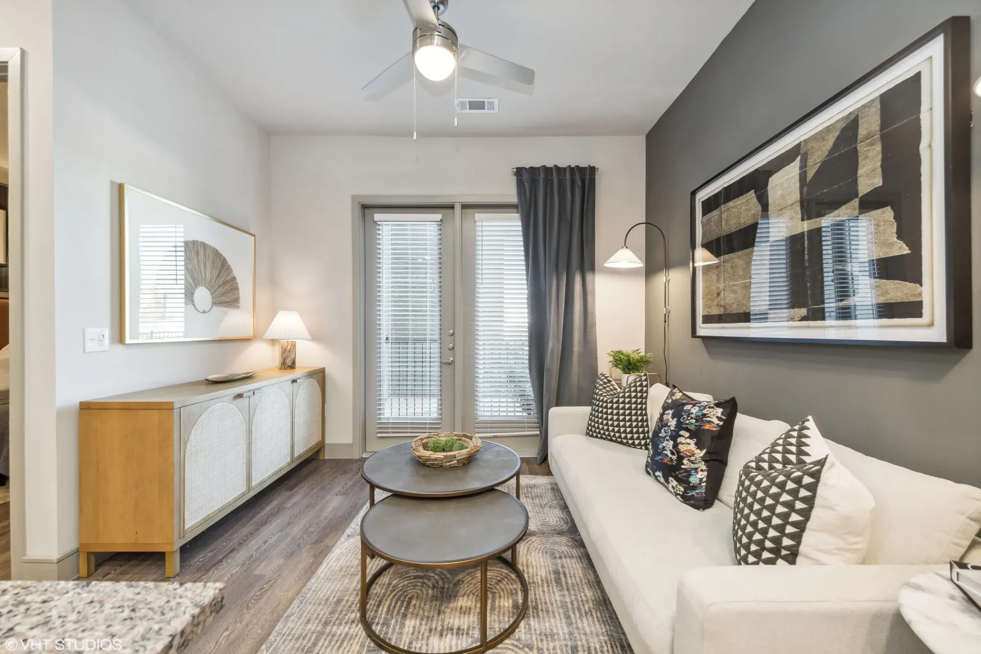 Living room in a modern apartment with a white sofa, two round coffee tables, art, and French doors.
