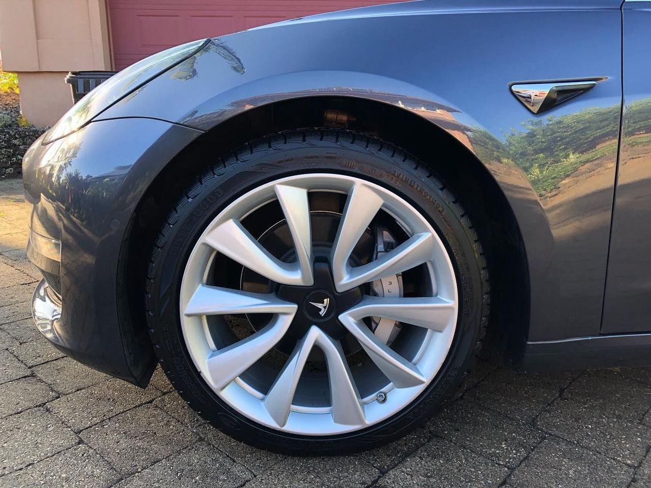 a tesla model 3 is parked in front of a red garage door