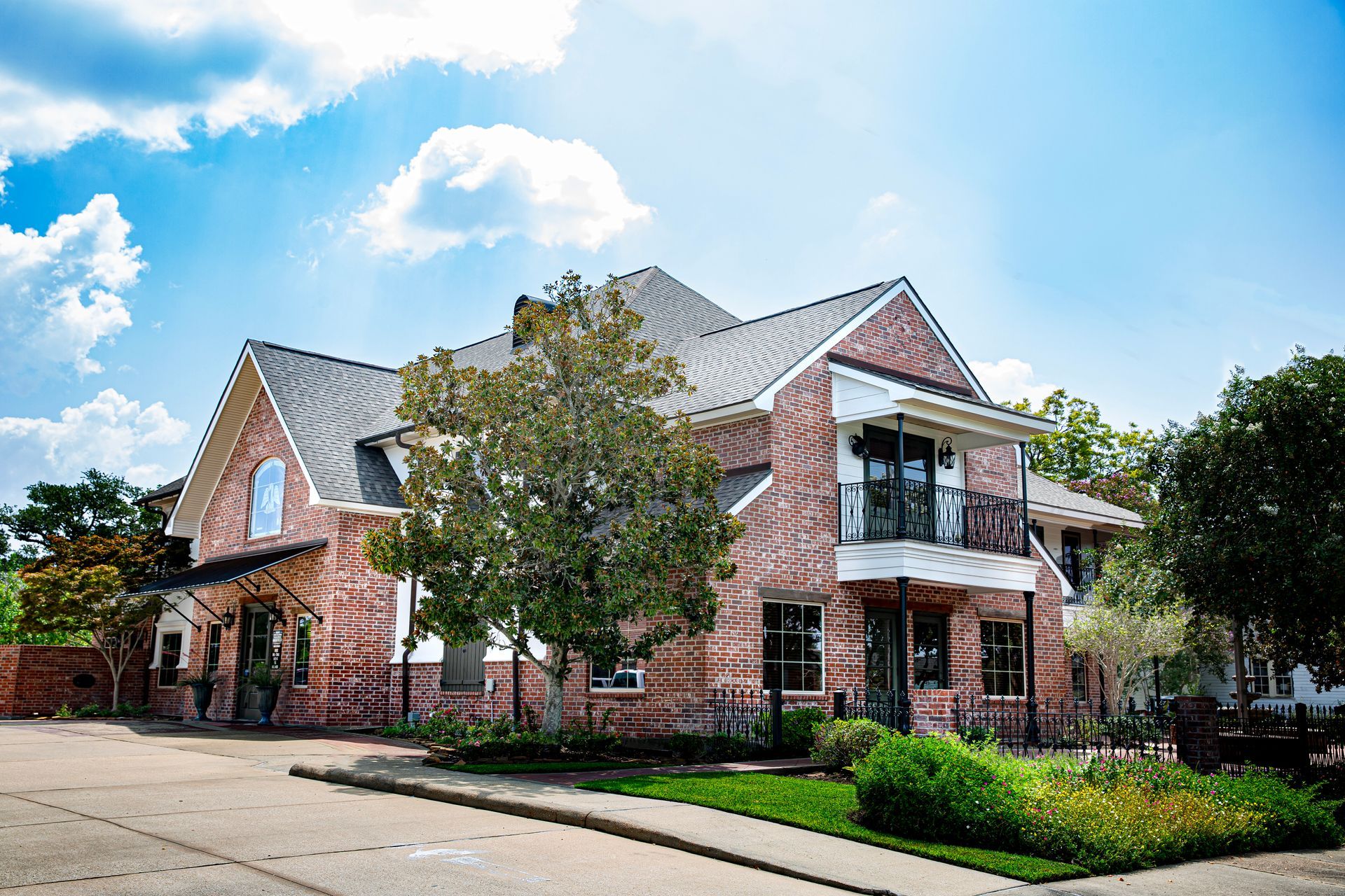 A large brick house with a gray roof is sitting on the corner of a street.