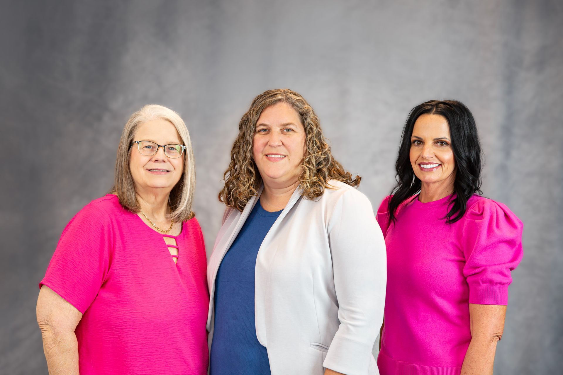 Three women in pink shirts are posing for a picture together.