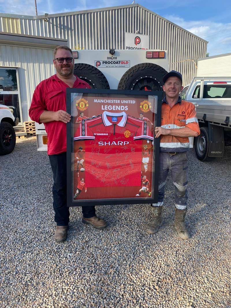 Two Procoat Men Are Standing Next To Each Other Holding A Framed Picture Of Manchester United T-shirt — Procoat QLD in Ryan, QLD