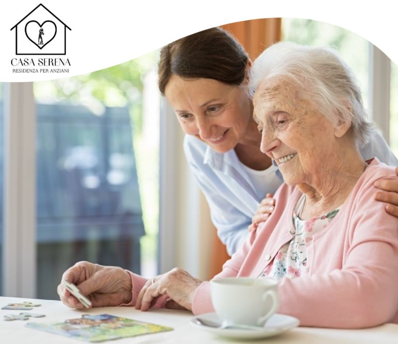 Una donna aiuta un anziano con un puzzle seduto a un tavolo in casa. Entrambi sorridono.