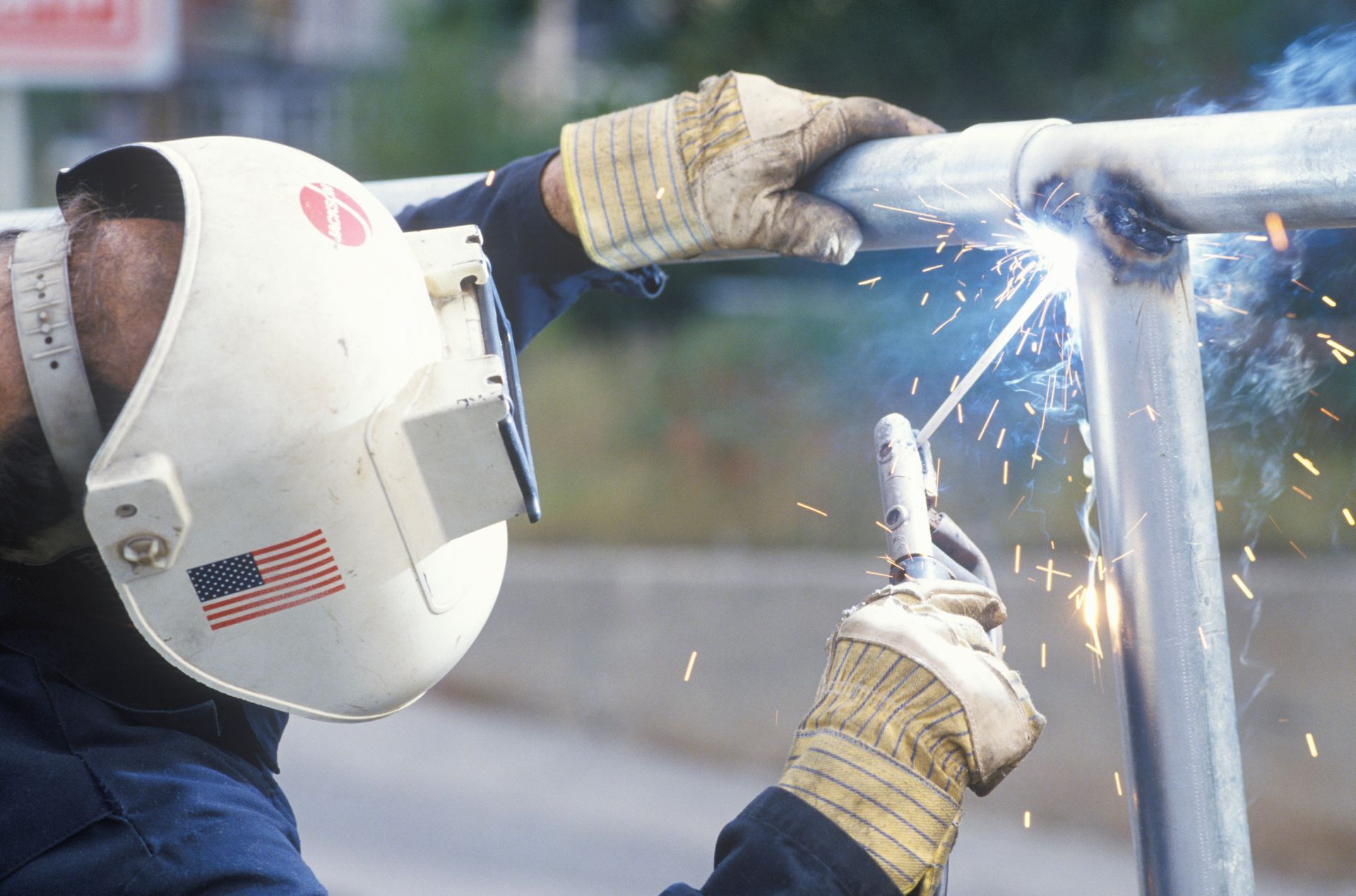 Welder in white helmet welds metal fences outdoors