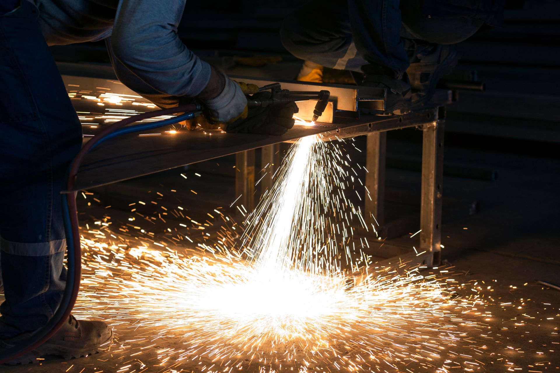 Person using a torch cutter, sparks flying as they cut through metal on a workbench
