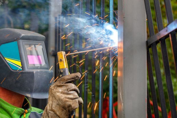 Welder wearing a mask, welding black metal fence with sparks Welder wearing a mask, welding black metal fence with sparks