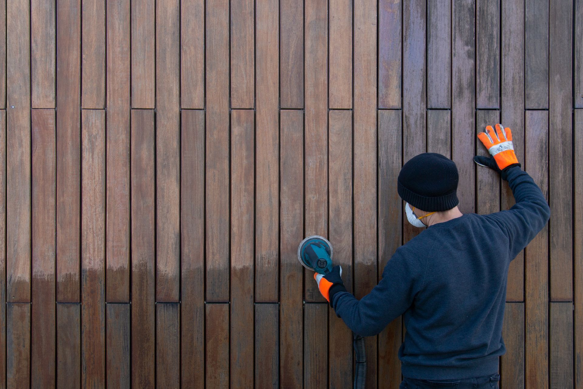 Person sanding a vertical wooden wall outdoors