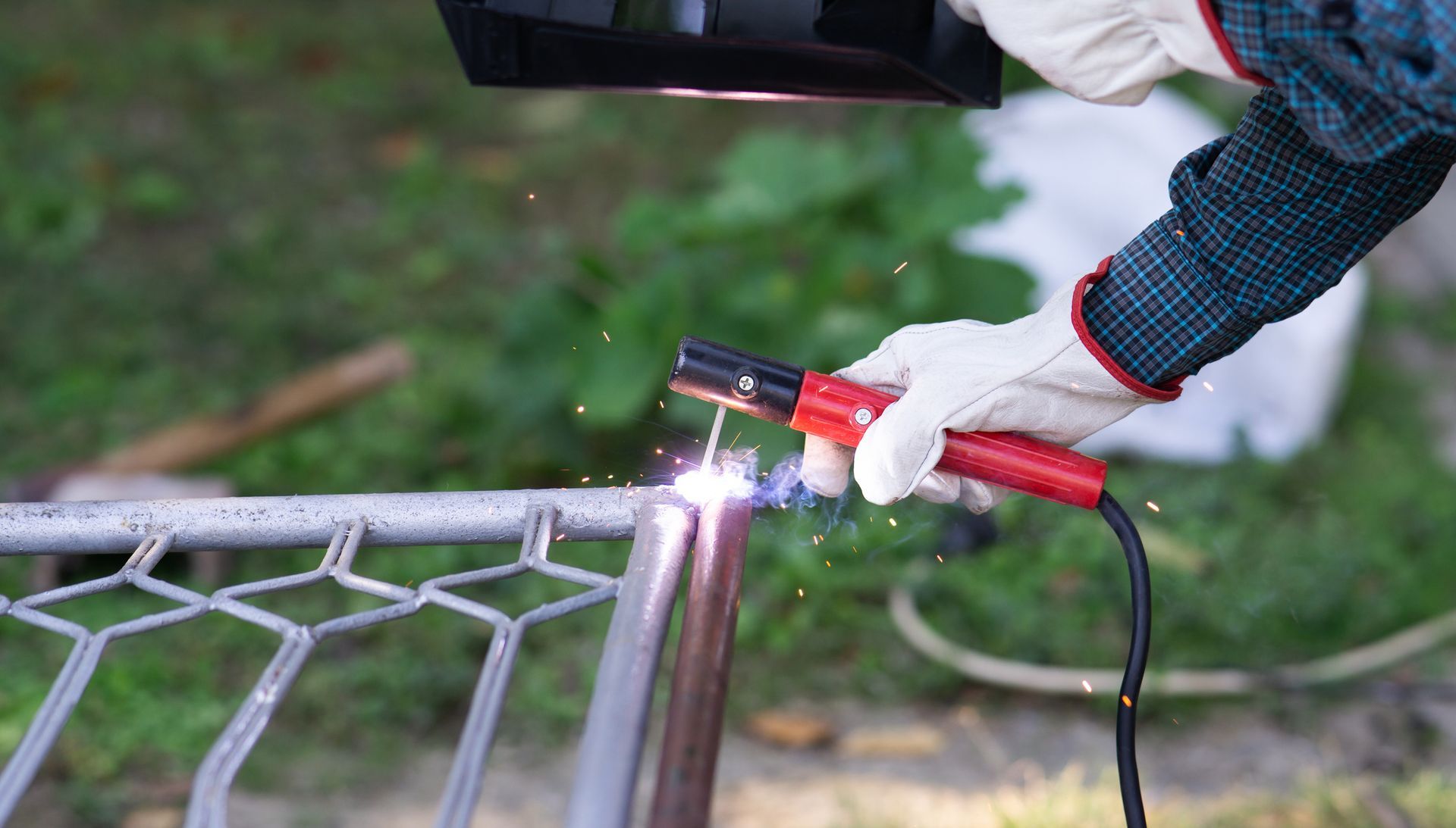 Welder welding metal fence, wearing gloves and a welding helmet outside