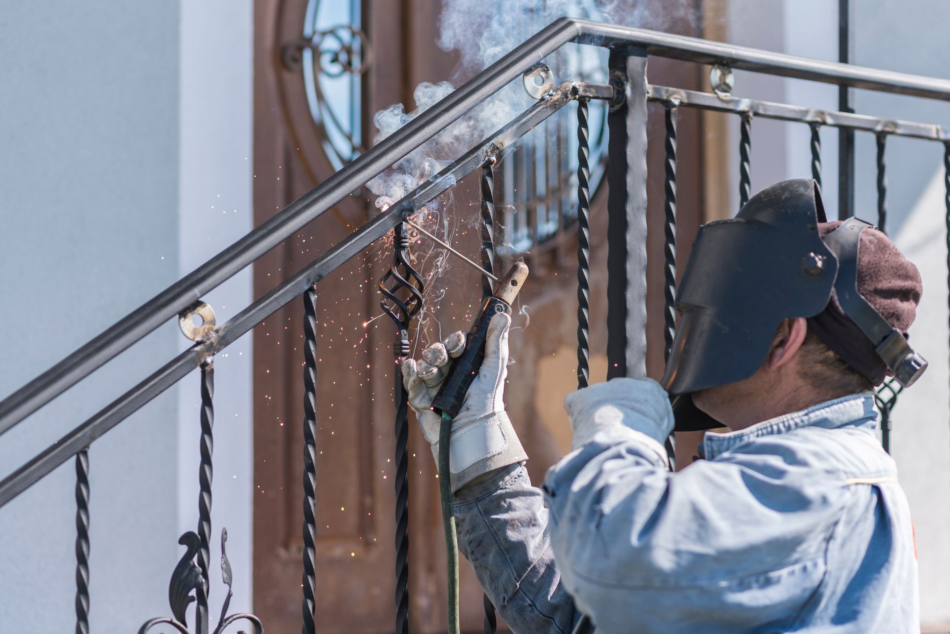 Welder wearing a face shield and gloves working on a metal railing