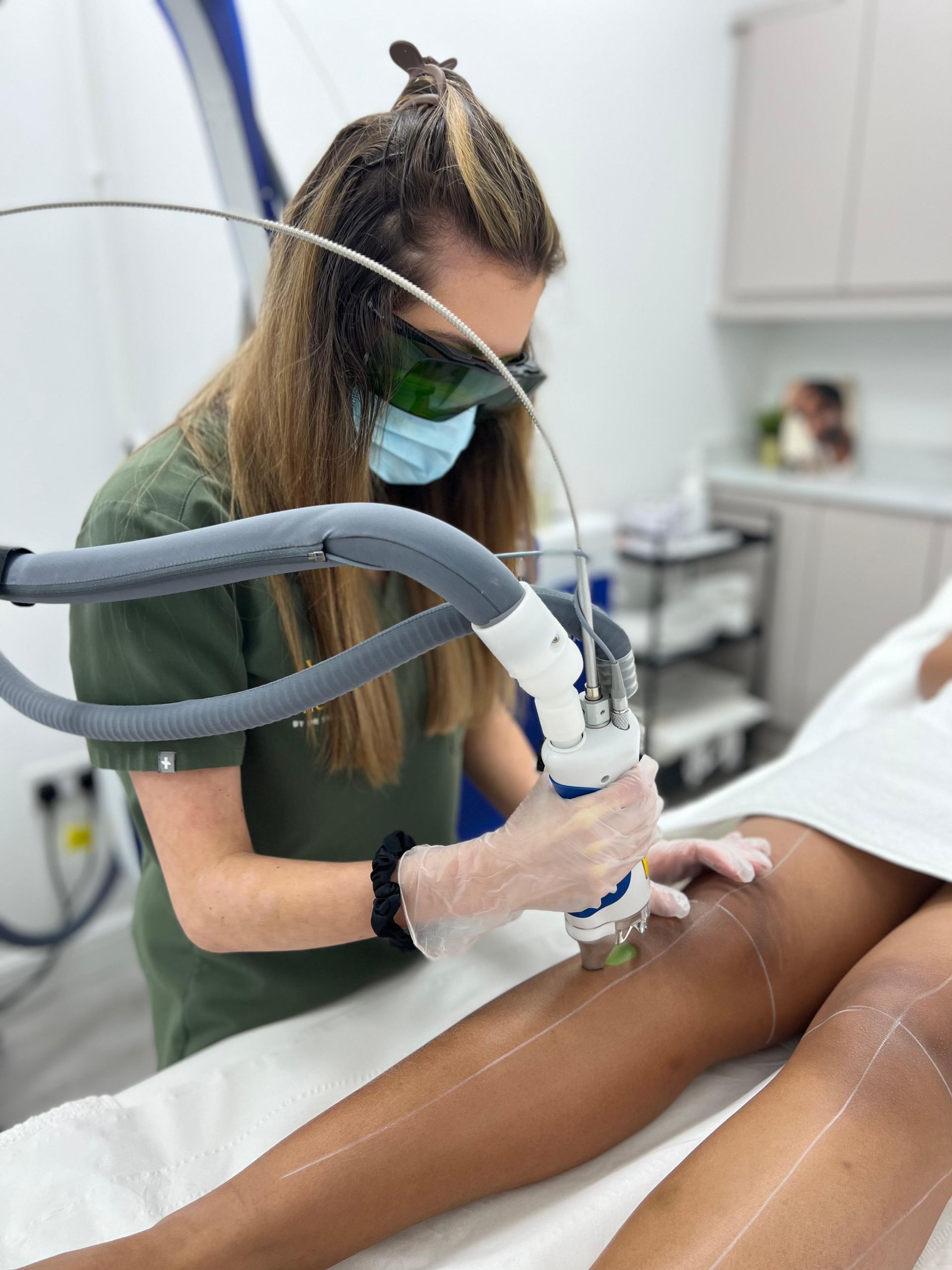 A woman is using a machine to remove hair from a woman 's leg.