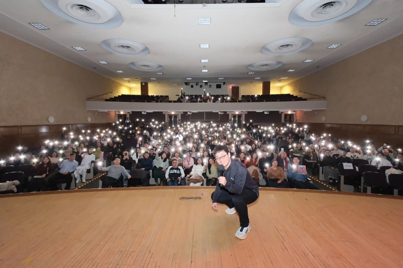 A man is squatting on a stage in front of a crowd