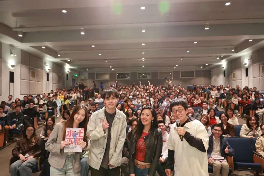 A group of people are standing in front of a crowd in a large auditorium.