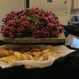 Table with a large pile of red grapes and assorted crackers on platters at a buffet