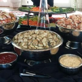 Buffet table with bowls of shrimp, dumplings, sauces, and vegetables on a black tablecloth