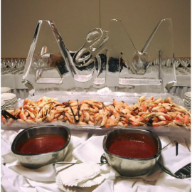 Ice sculpture centerpiece behind shrimp trays and bowls of red cocktail sauce on a buffet table