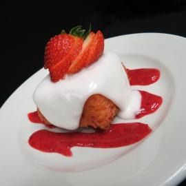 Dessert topped with whipped cream and strawberry slices on a white plate with red sauce drizzle