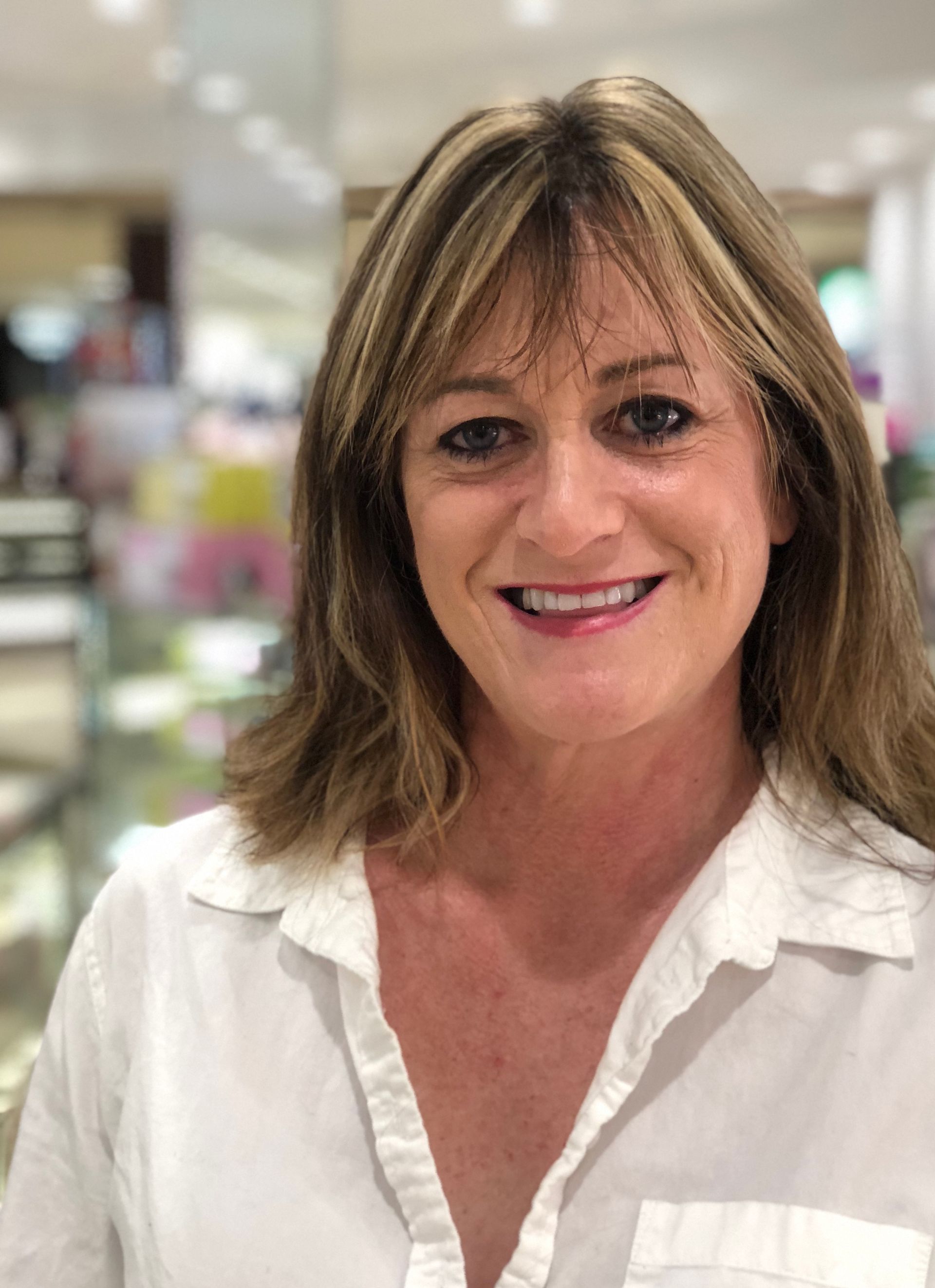 A woman in a white shirt is smiling for the camera in a store.