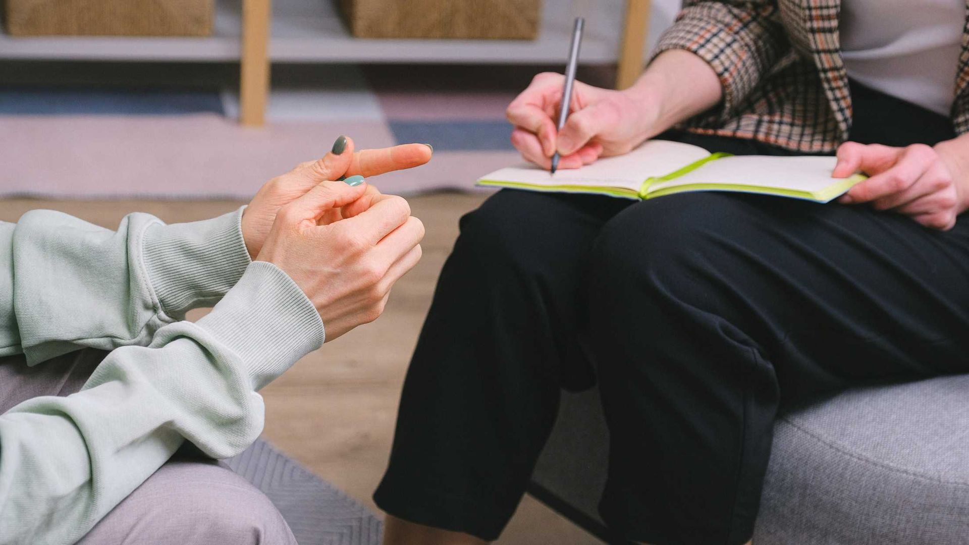 A woman is sitting on a couch talking to a man who is writing in a notebook.