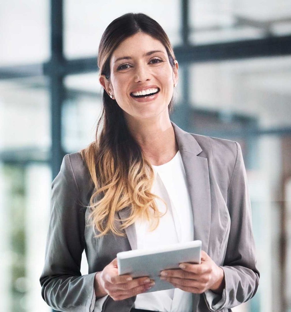A woman in a suit is holding a tablet and smiling.